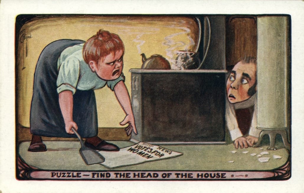 Image is a postcard that shows a woman bending down to pick up a paper that reads "votes for women." Behind the woman is a table, and there's a man, presumably her husband, crouched behind it looking at the woman with a scared facial expression.