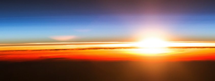 "Sunrise at the International Space Station" from NASA. Image description: a vertical rectangle showing a dramatic sunrise, with the bottom half of the image black. The sunrise is shown as bands of color: red, orange, yellow, with the sun at the right side of the image. Above the sun is a gradient blue sky with a light blue band surrounding the sun and progressively darker blue toward the top of the image. In the bottom left corner is the word Peitho in a sans-serif font in a sunrise gradient. Underneath that are the words "Volume 24.1 Fall 2021."