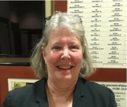 Kathleen Yancey smiles at the camera and poses in front of a red and white wall