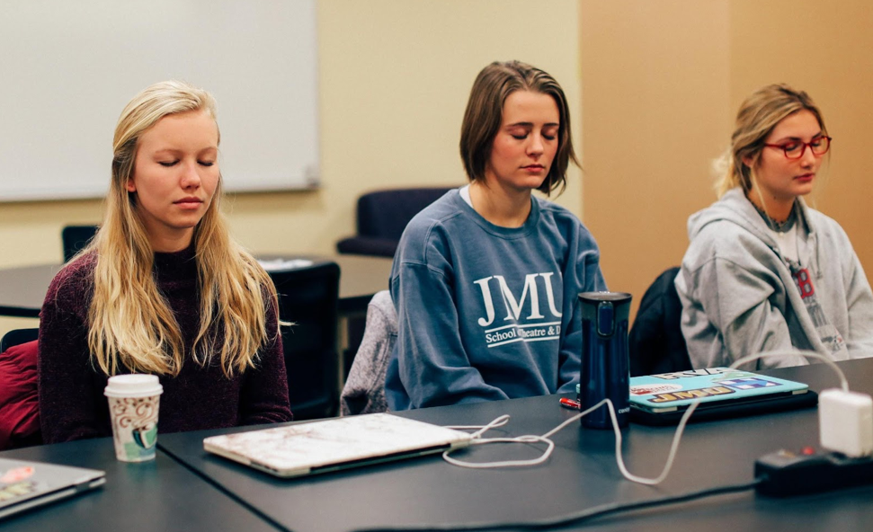 Photo of three James Madison University students sit in meditation with their eyes closed during their tutor education course.