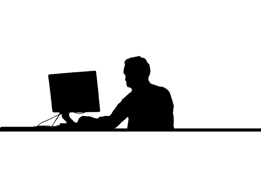 Silhouette of person working on a desktop computer.